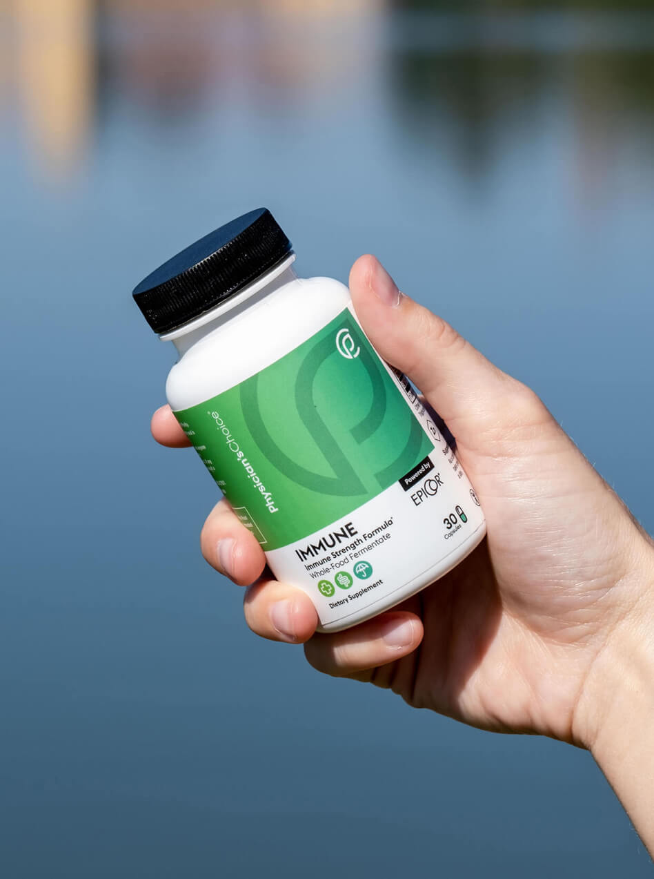 Picture of a hand holding an immune system supplement with a lake in the background.